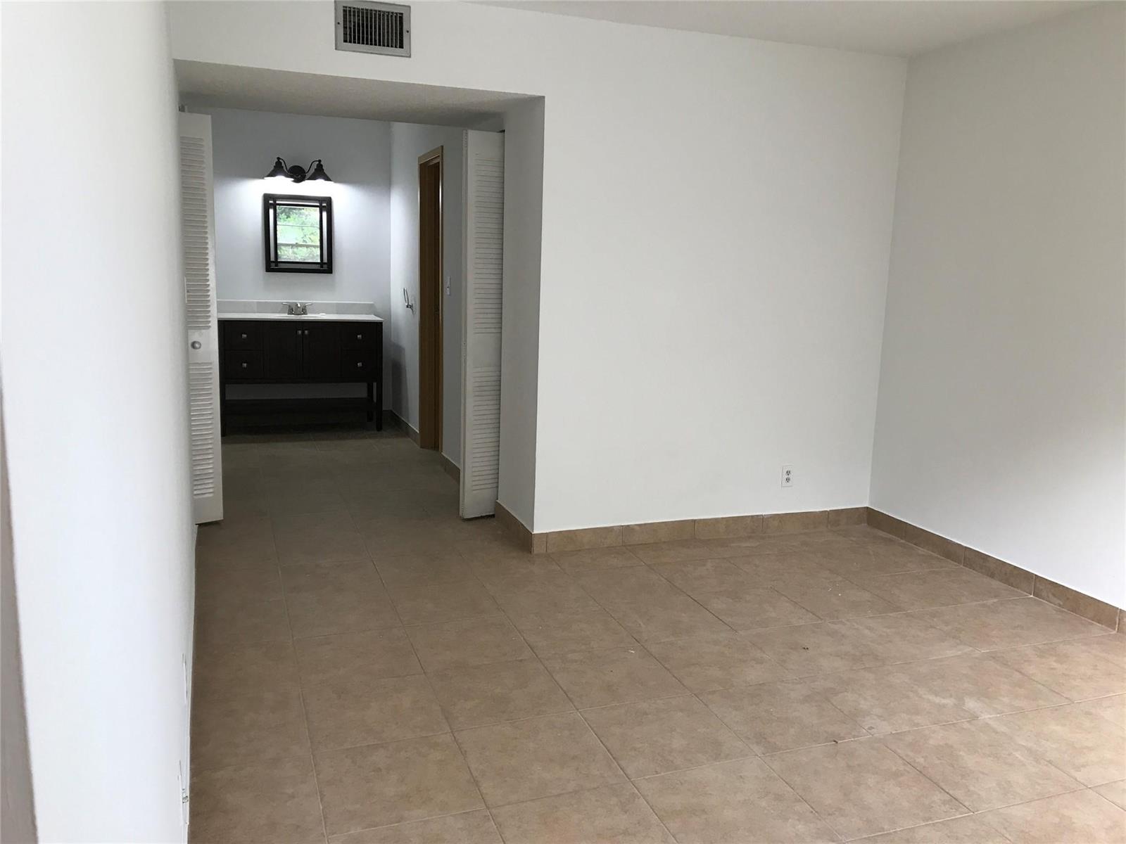 A room with tan tile flooring leads into a bathroom featuring a dark wood vanity — 4394 NW 9th Avenue # 3a, Deerfield Beach FL 33064, DEERFIELD BEACH, FL
