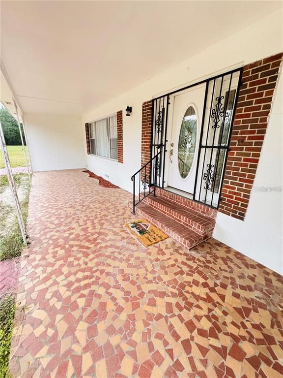A covered porch features a mosaic tile floor, brick steps, and a white front door — 2022 EDGEWOOD ROAD, LEESBURG, FL