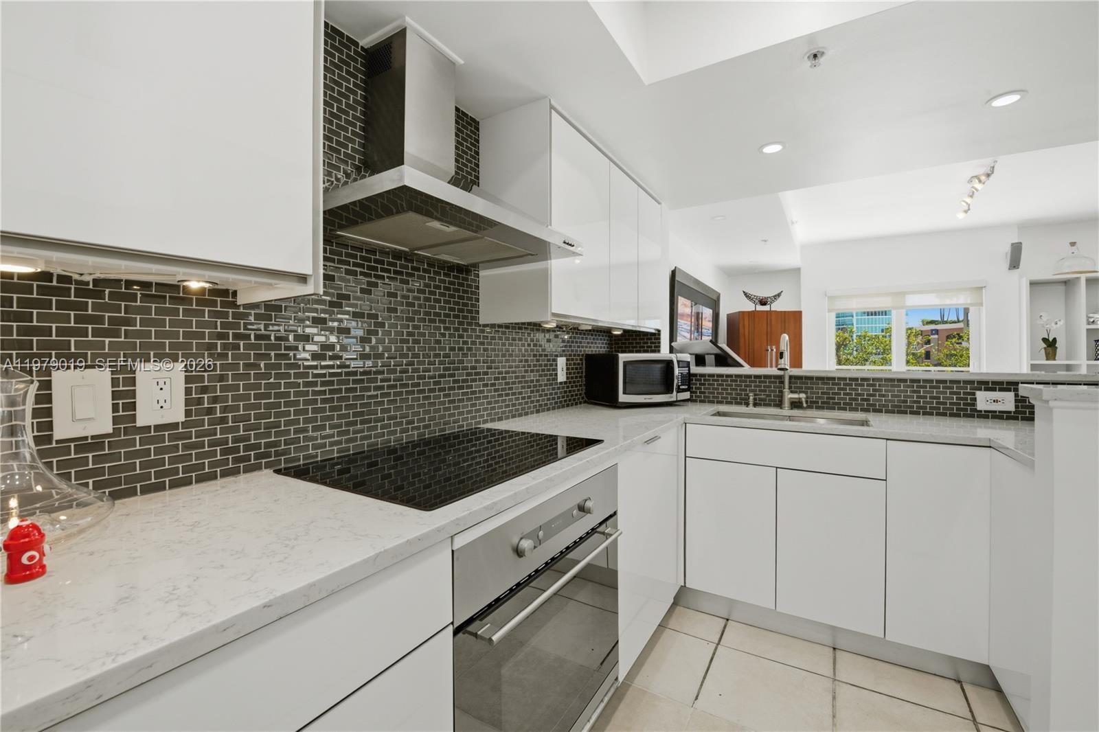 A modern kitchen features white cabinets, a dark tiled backsplash, and stainless steel appliances — 120 Jefferson Ave # 12022, Miami Beach FL 33139, MIAMI BEACH, FL
