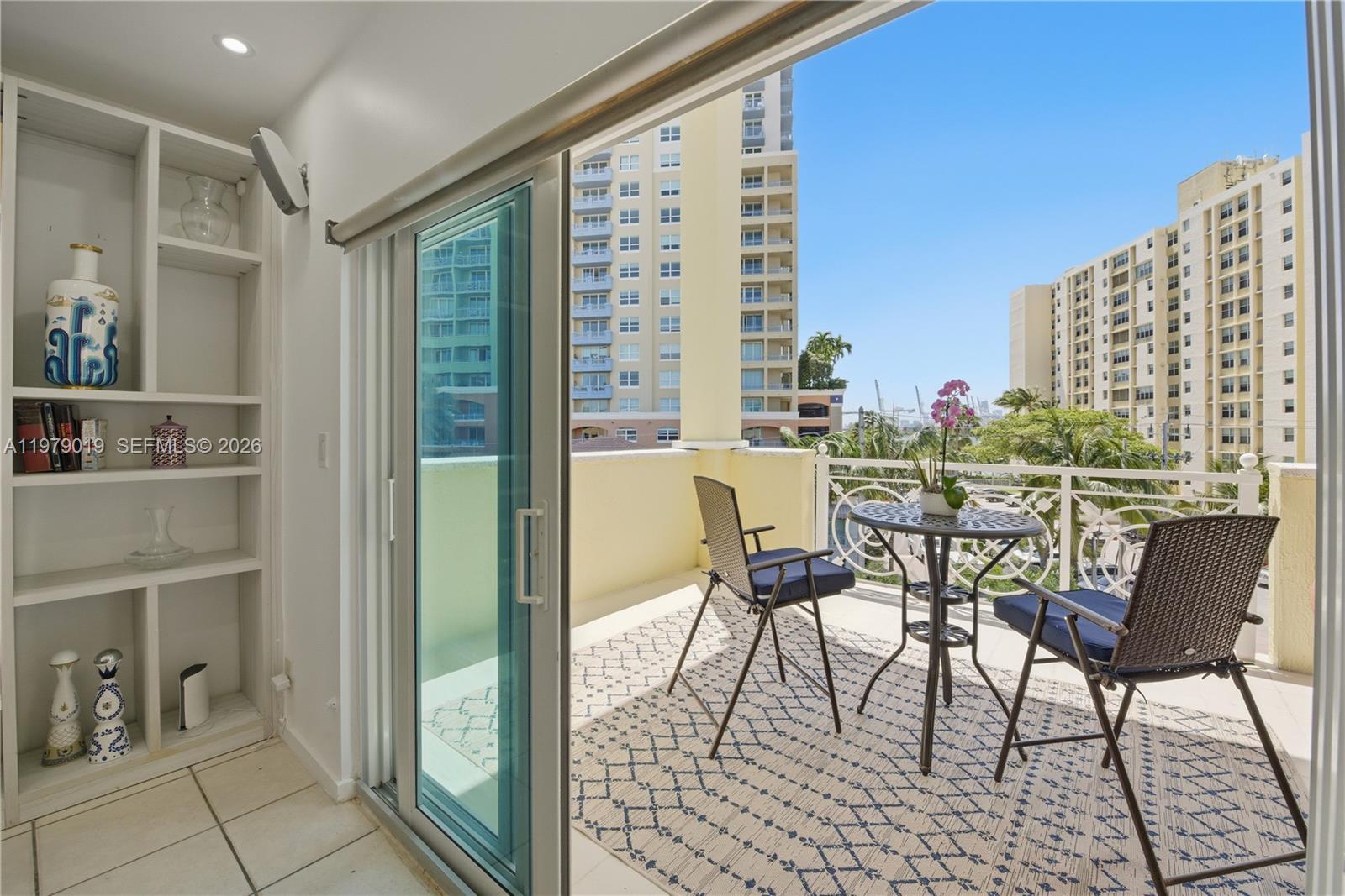 A balcony with a table and chairs overlooks a city view from a sliding door — 120 Jefferson Ave # 12022, Miami Beach FL 33139, MIAMI BEACH, FL