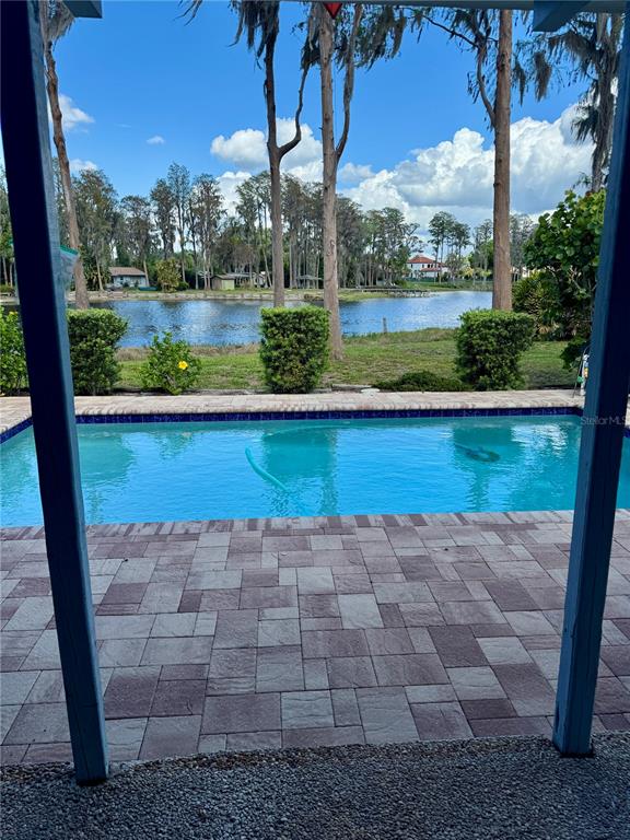 A swimming pool sits on a paved patio overlooking a lake and trees — 17109 RAINBOW TERRACE, ODESSA, FL