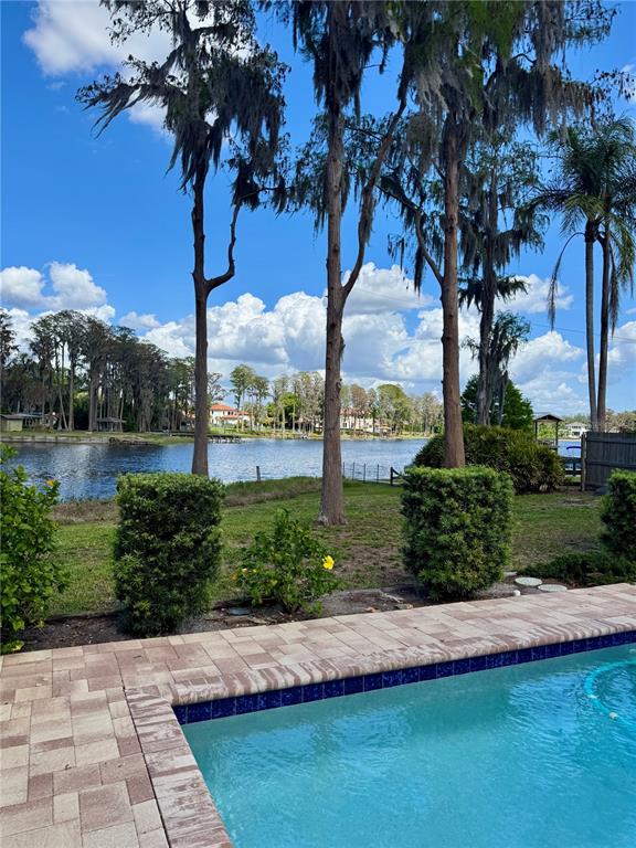 A swimming pool overlooks a lake framed by tall trees under a blue sky — 17109 RAINBOW TERRACE, ODESSA, FL
