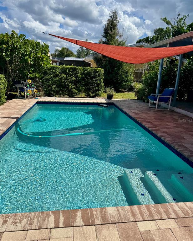 A rectangular swimming pool with steps is surrounded by a brick paver deck and shade sail — 17109 RAINBOW TERRACE, ODESSA, FL