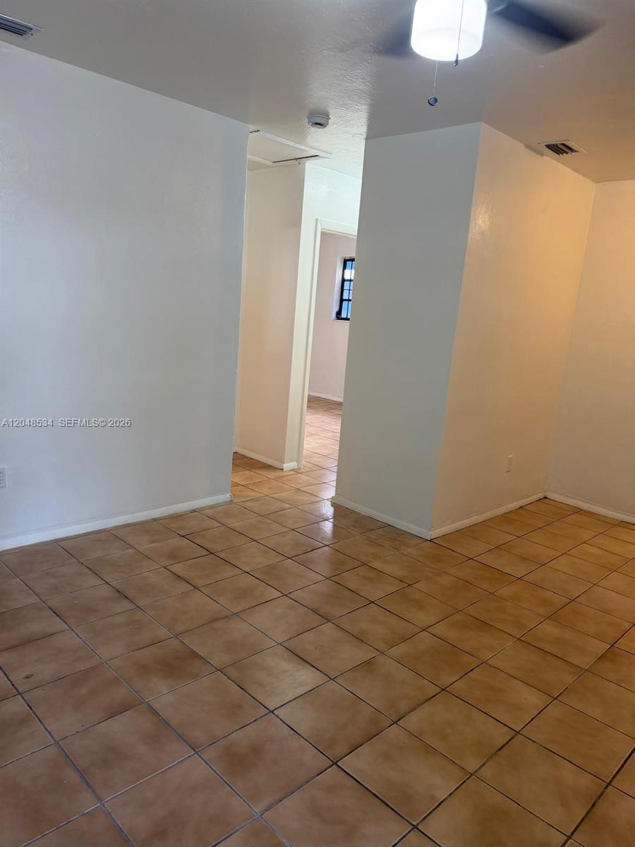 A room with light-colored walls and tan tile flooring leads to a hallway — 1019 NW 52nd St # A, Miami FL 33127, MIAMI, FL
