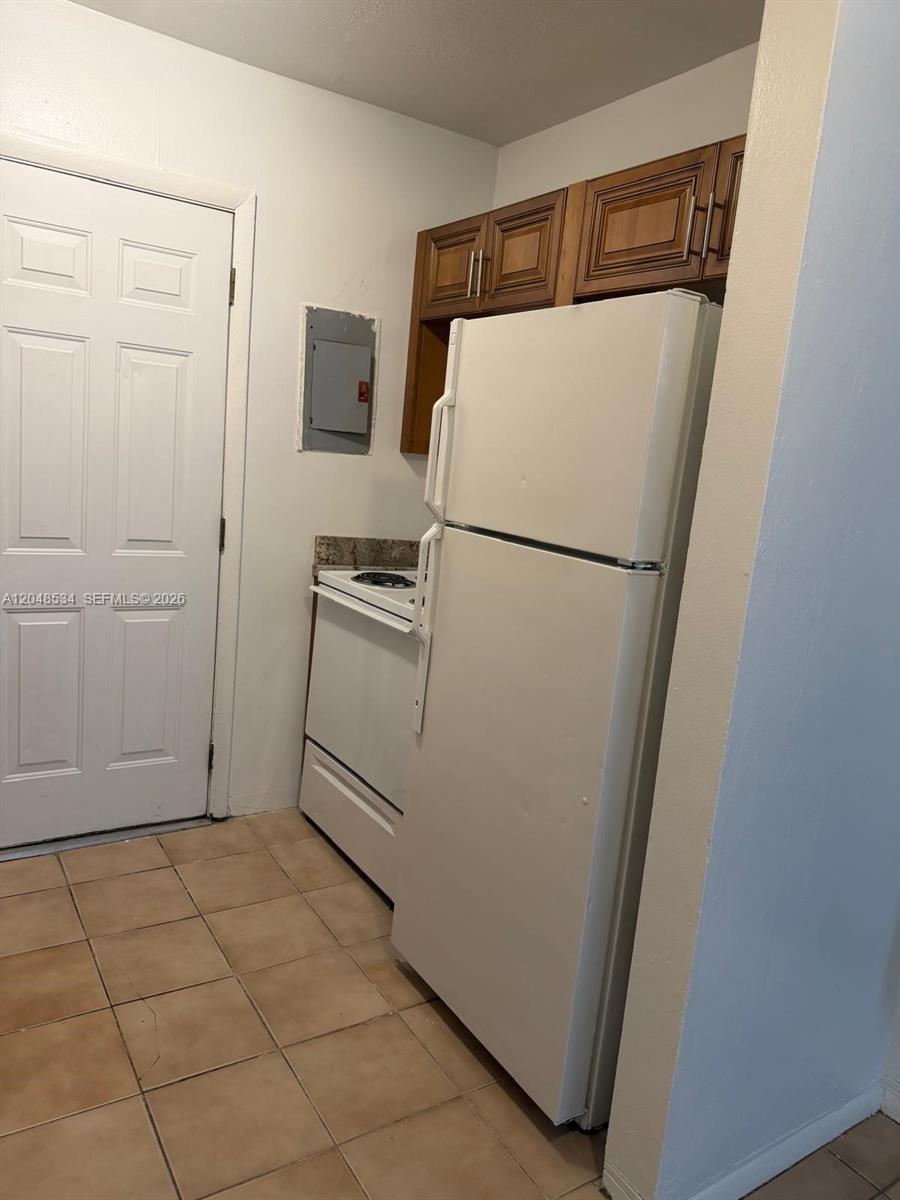 A small kitchen features a white refrigerator, a stove, and wooden upper cabinets — 1019 NW 52nd St # A, Miami FL 33127, MIAMI, FL