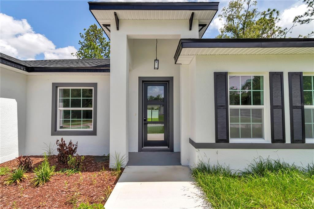 A modern white house exterior features a dark-framed front door, shutters, and a concrete walkway — 2433 W ANDROMEDAE DRIVE, CITRUS SPRINGS, FL