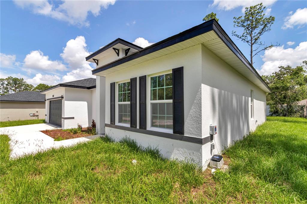 A white house with a black roof and dark window shutters sits on a lawn — 2433 W ANDROMEDAE DRIVE, CITRUS SPRINGS, FL