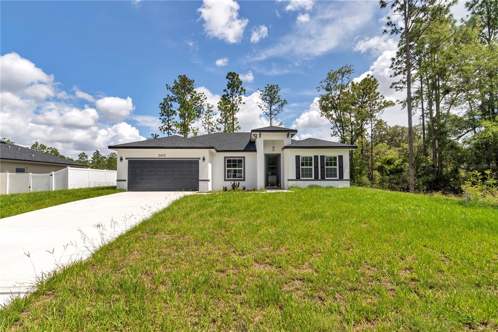 A single-story house with a white stucco exterior, dark roof, and a two-car garage — 2433 W ANDROMEDAE DRIVE, CITRUS SPRINGS, FL