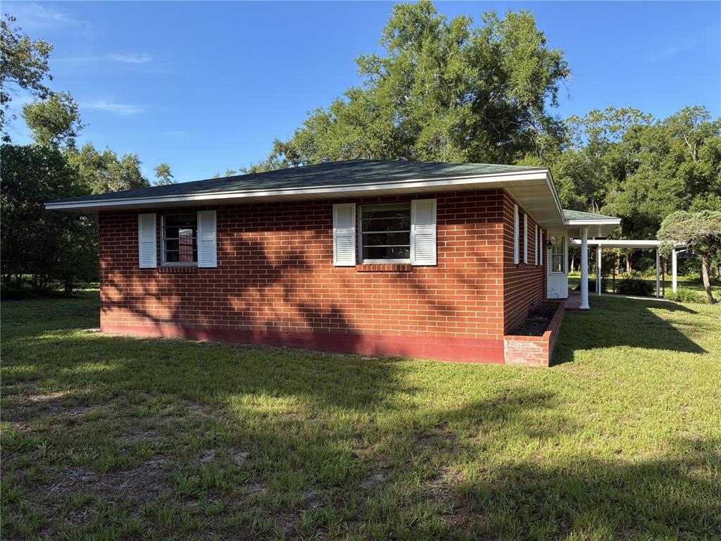 A single-story red brick house with white shutters, a green roof, and a side carport — 4926 MAGNOLIA RIDGE ROAD, FRUITLAND PARK, FL