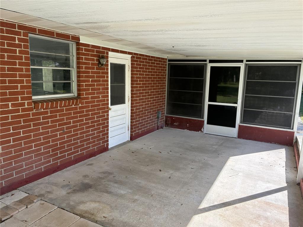 A covered concrete patio features a brick wall, a white door, and a screened enclosure — 4926 MAGNOLIA RIDGE ROAD, FRUITLAND PARK, FL