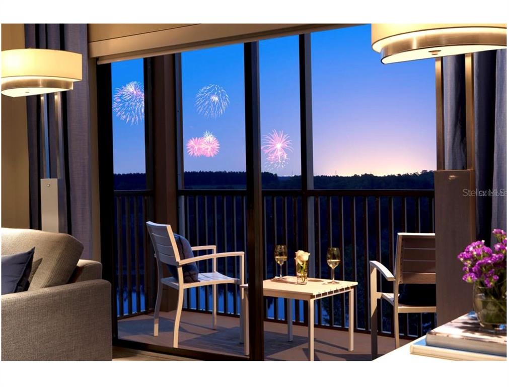 A balcony with two chairs and a table overlooks a landscape with fireworks at dusk — 14501 GROVE RESORT AVENUE UNIT 1237, WINTER GARDEN, FL