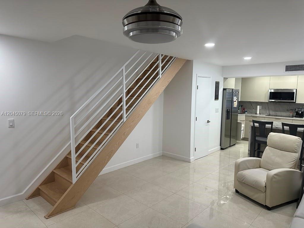 A staircase with white railings and wood treads stands next to a modern kitchen — 1560 W 46th St # 228, Hialeah FL 33012, HIALEAH, FL