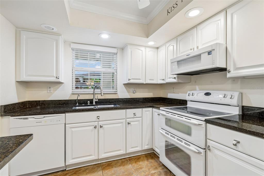 A kitchen with white cabinets, dark countertops, white appliances, and a window above the sink — 10387 CARROLLWOOD LANE UNIT 303, TAMPA, FL