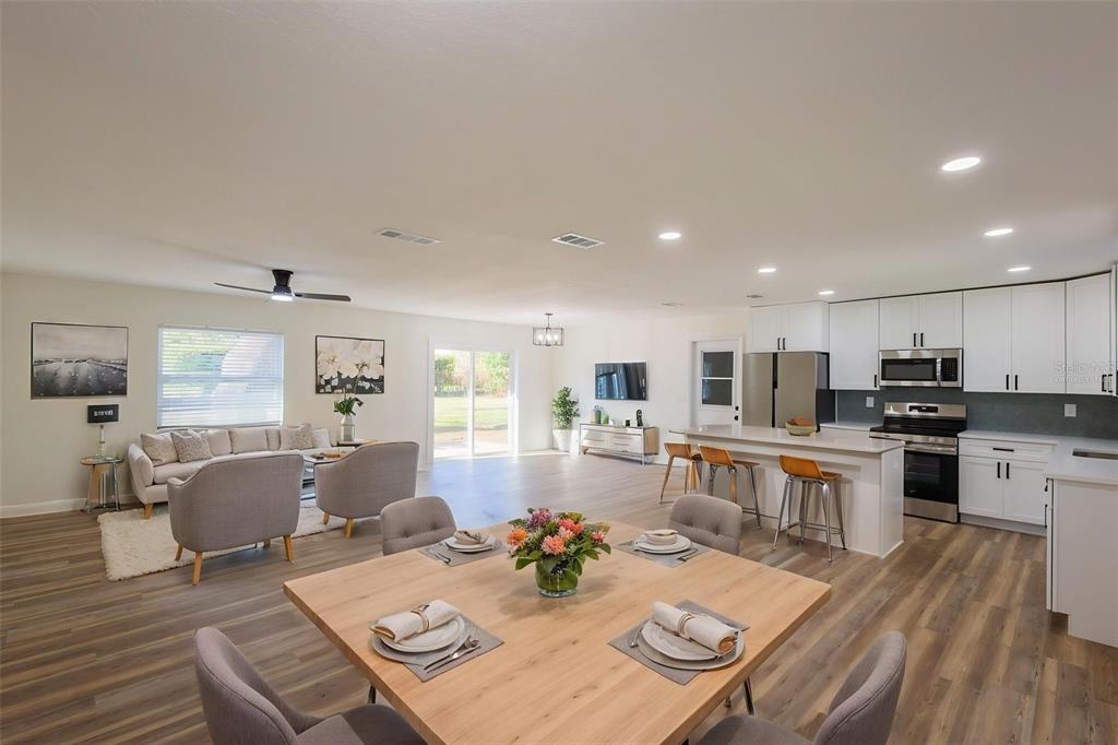 An open-concept living, dining, and kitchen area with light wood floors and white cabinetry — 1517 HALLAM COURT N, LAKELAND, FL