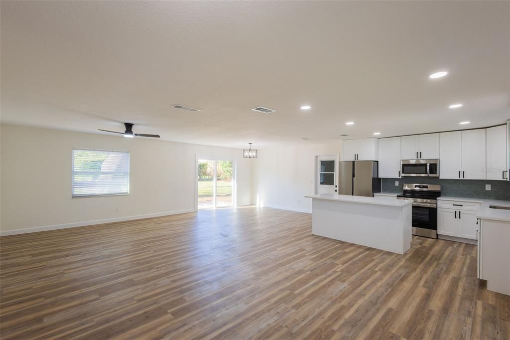 An open-concept kitchen and living area features white cabinets, stainless appliances, and wood-look flooring — 1517 HALLAM COURT N, LAKELAND, FL