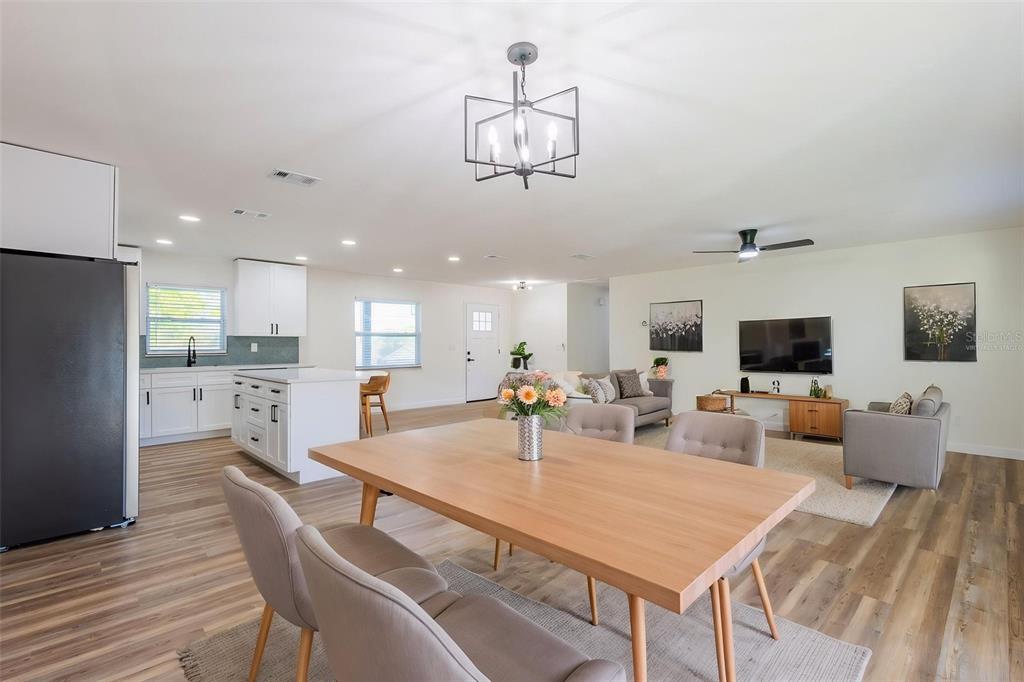 An open-concept living area features a kitchen with white cabinets, a dining table, and furniture — 1517 HALLAM COURT N, LAKELAND, FL
