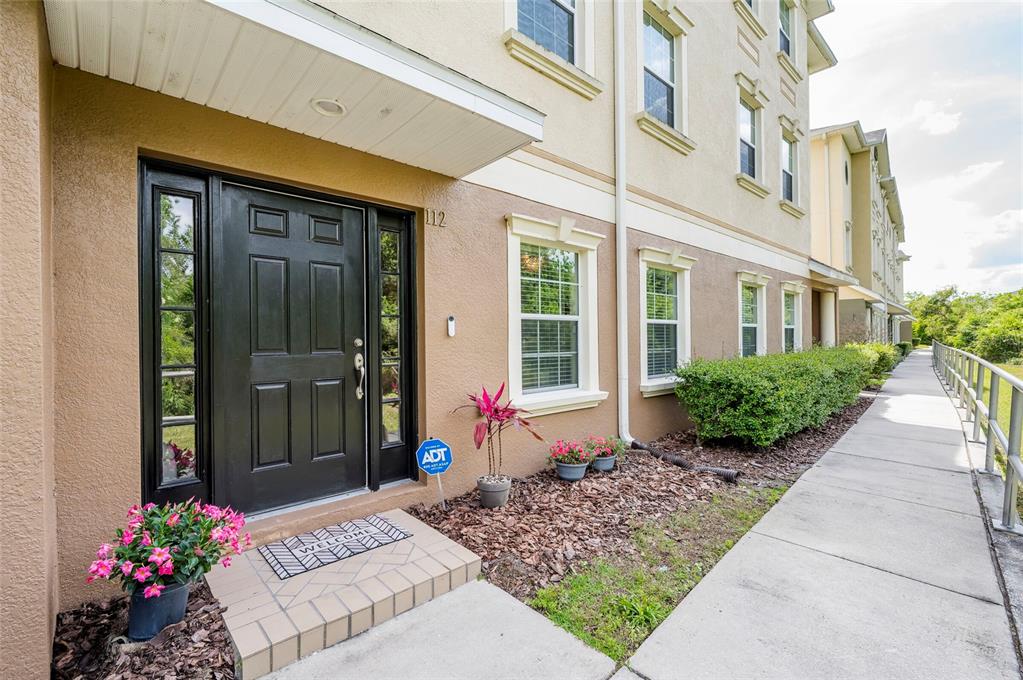 A tan building exterior features a black front door, a walkway, and small potted plants — 10144 ARBOR RUN DRIVE UNIT 112, TAMPA, FL