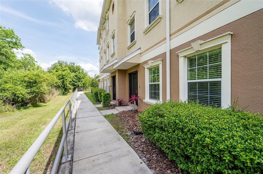 A concrete walkway runs alongside a multi-story townhouse with tan stucco walls and landscaping — 10144 ARBOR RUN DRIVE UNIT 112, TAMPA, FL