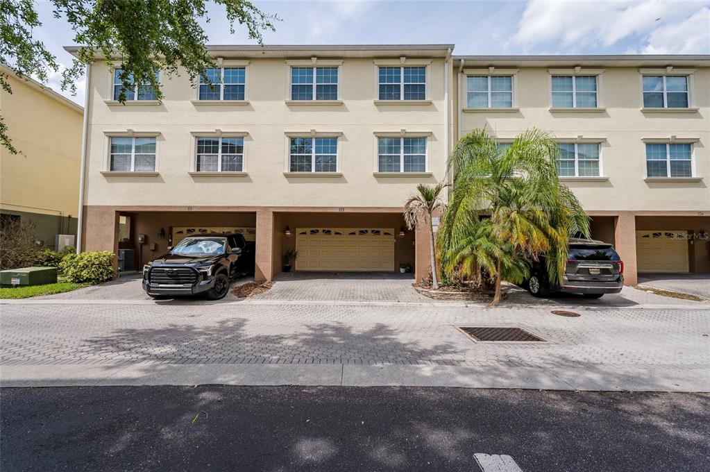 A three-story townhouse exterior features tan stucco walls, multiple windows, and ground-level garage bays — 10144 ARBOR RUN DRIVE UNIT 112, TAMPA, FL