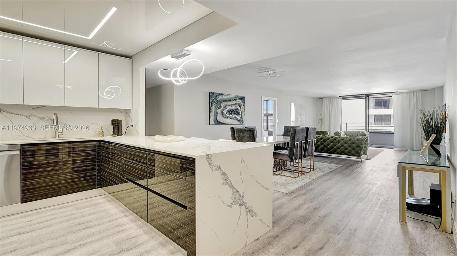 A modern kitchen with dark wood cabinets and a white marble island opens to a living area — 2500 Parkview Dr # 1914, Hallandale Beach FL 33009, HALLANDALE BEACH, FL