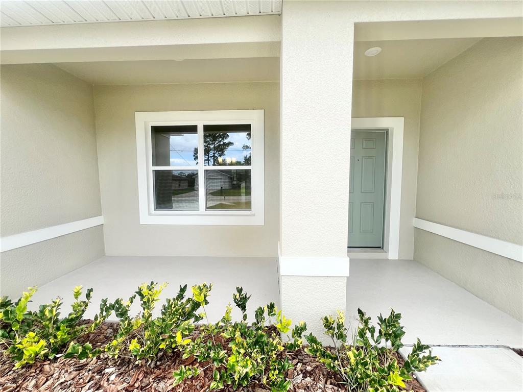 A covered front porch features a light-colored door, a window, and a landscaped garden bed — 101 PRITCHARD DRIVE, PALM COAST, FL