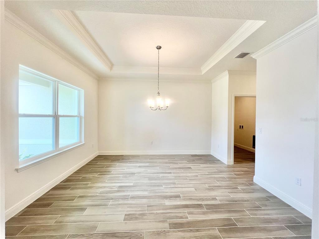 An empty dining room features a tray ceiling, a chandelier, and wood-look tile flooring — 101 PRITCHARD DRIVE, PALM COAST, FL
