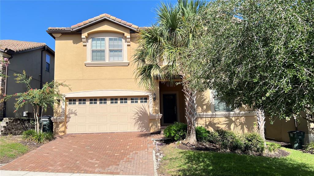 A two-story tan stucco house features a brick driveway, a garage, and a palm tree — 1908 NICE COURT, KISSIMMEE, FL