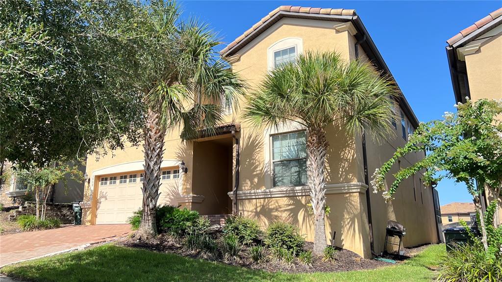 A two-story tan stucco house features a two-car garage and two palm trees — 1908 NICE COURT, KISSIMMEE, FL