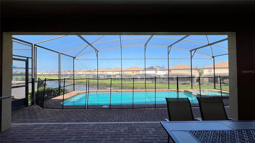 A covered patio with a brick floor overlooks a screened-in swimming pool and lake — 1908 NICE COURT, KISSIMMEE, FL