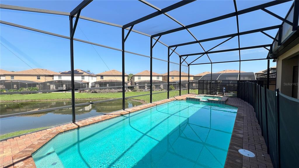 A screened-in swimming pool and spa overlook a pond behind a residential home — 1908 NICE COURT, KISSIMMEE, FL