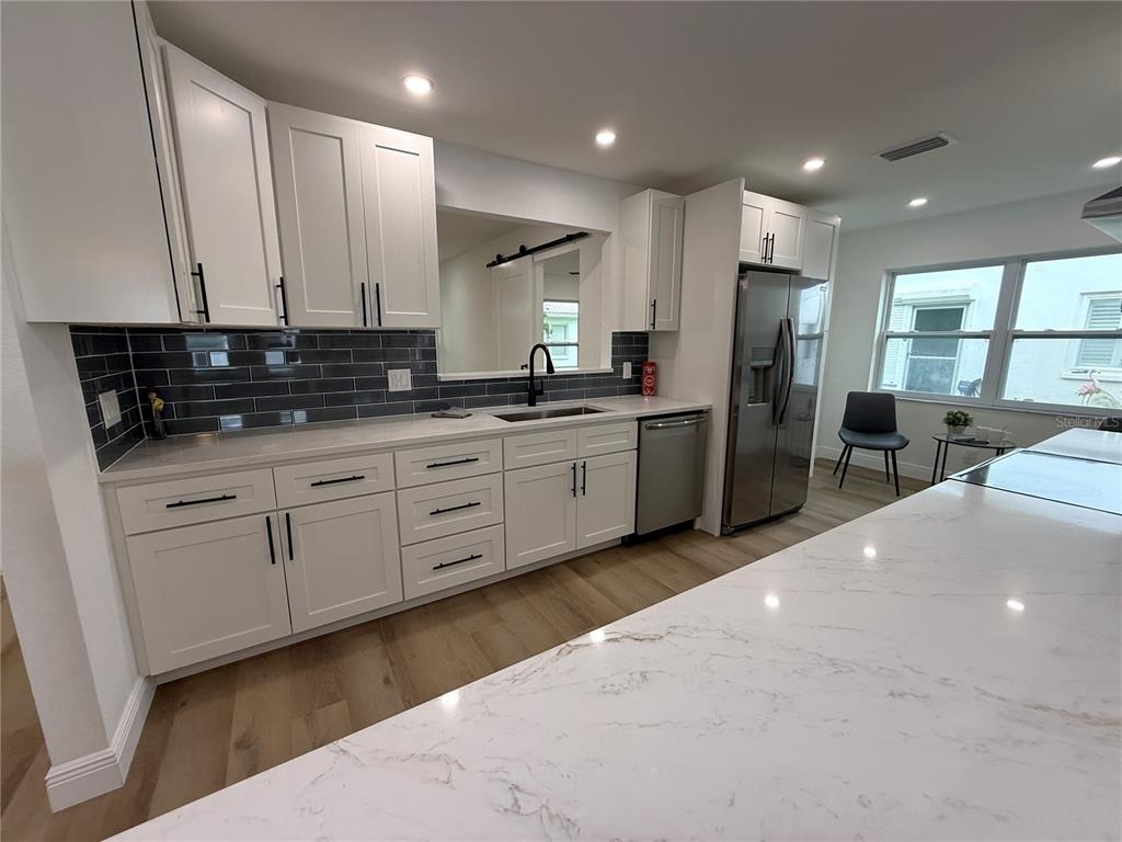 An open-concept living room and kitchen feature light wood flooring, gray furniture, and recessed lighting — 9124 39TH LANE N, PINELLAS PARK, FL