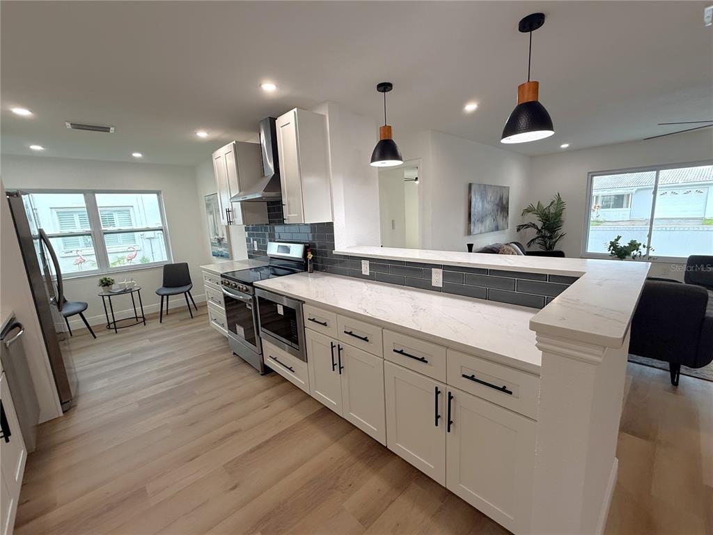A bright, open-concept kitchen and living area featuring white cabinets, wood flooring, and pendant lighting — 9124 39TH LANE N, PINELLAS PARK, FL