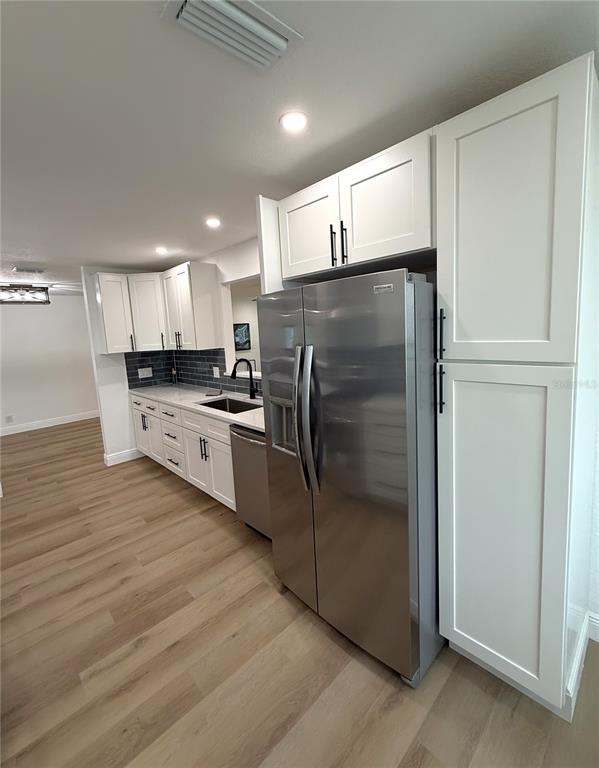 A kitchen features white cabinets, stainless steel appliances, gray subway tile backsplash, and wood flooring — 9124 39TH LANE N, PINELLAS PARK, FL