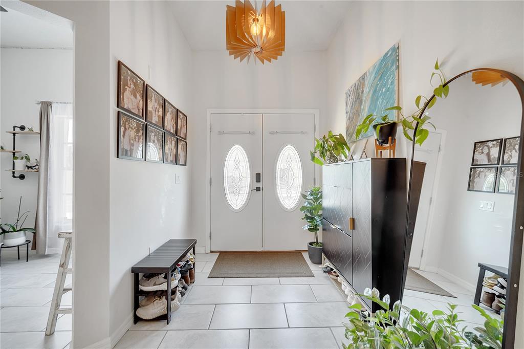 A bright entryway features white walls, tiled floors, a double front door, and modern decor — 1028 UNIVERSAL REST PLACE, KISSIMMEE, FL