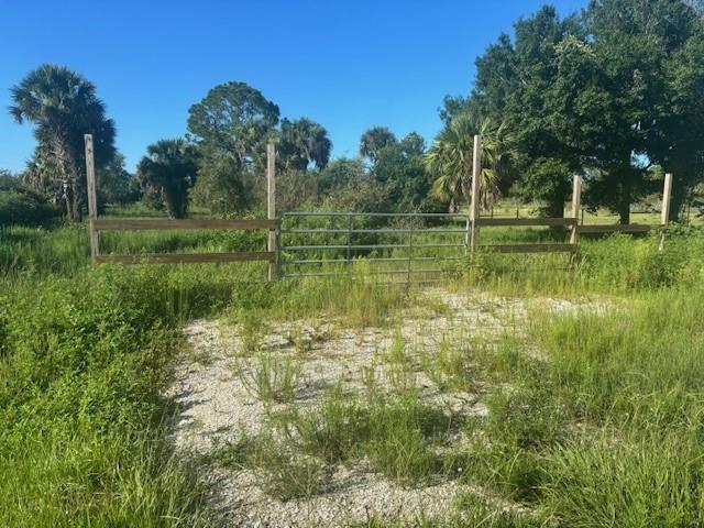 A metal gate and wooden fence enclose a gravel driveway surrounded by grass and trees — 19216 NW 300th Street, Okeechobee FL 34972, OKEECHOBEE, FL