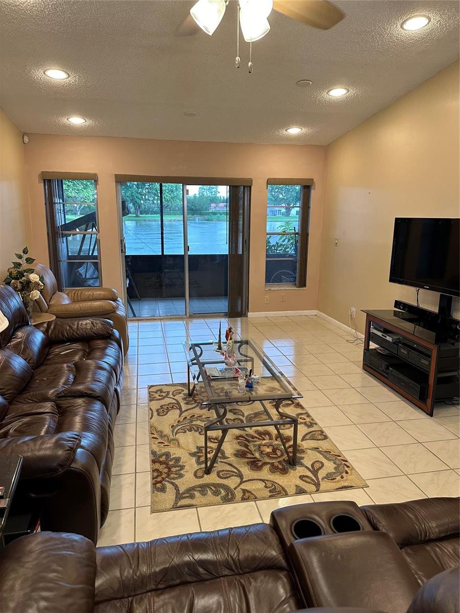 A living room with tile floors, brown leather furniture, a glass coffee table, and sliding doors — 8885 Windtree Street # D, Boca Raton FL 33496, BOCA RATON, FL