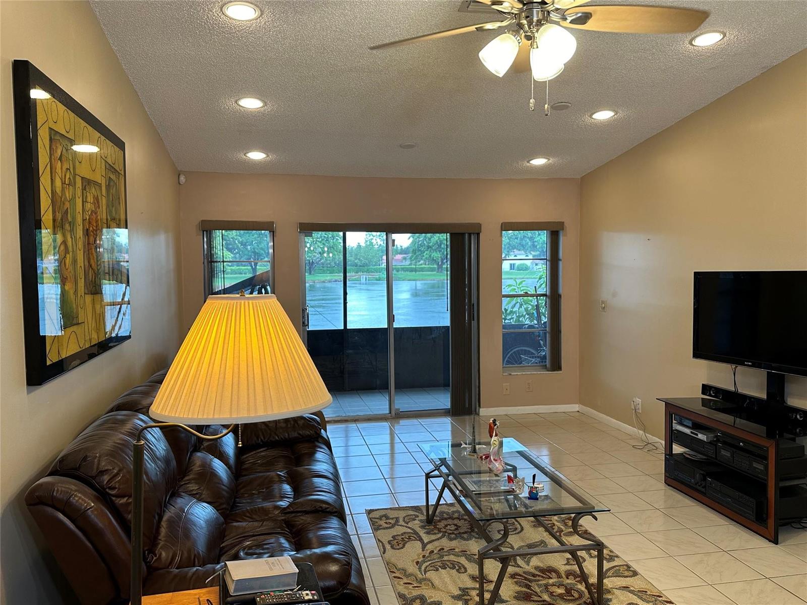 A living room features a leather sofa, glass coffee table, and sliding doors overlooking water — 8885 Windtree Street # D, Boca Raton FL 33496, BOCA RATON, FL
