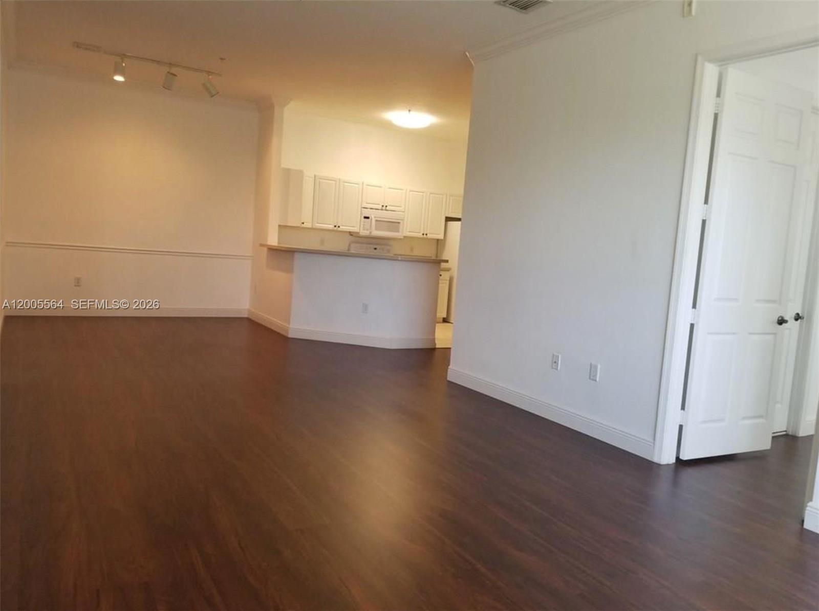 A living room with dark wood-look flooring leads to an open kitchen with white cabinets — 4508 SW 160th Ave # 736, Miramar FL 33027, MIRAMAR, FL