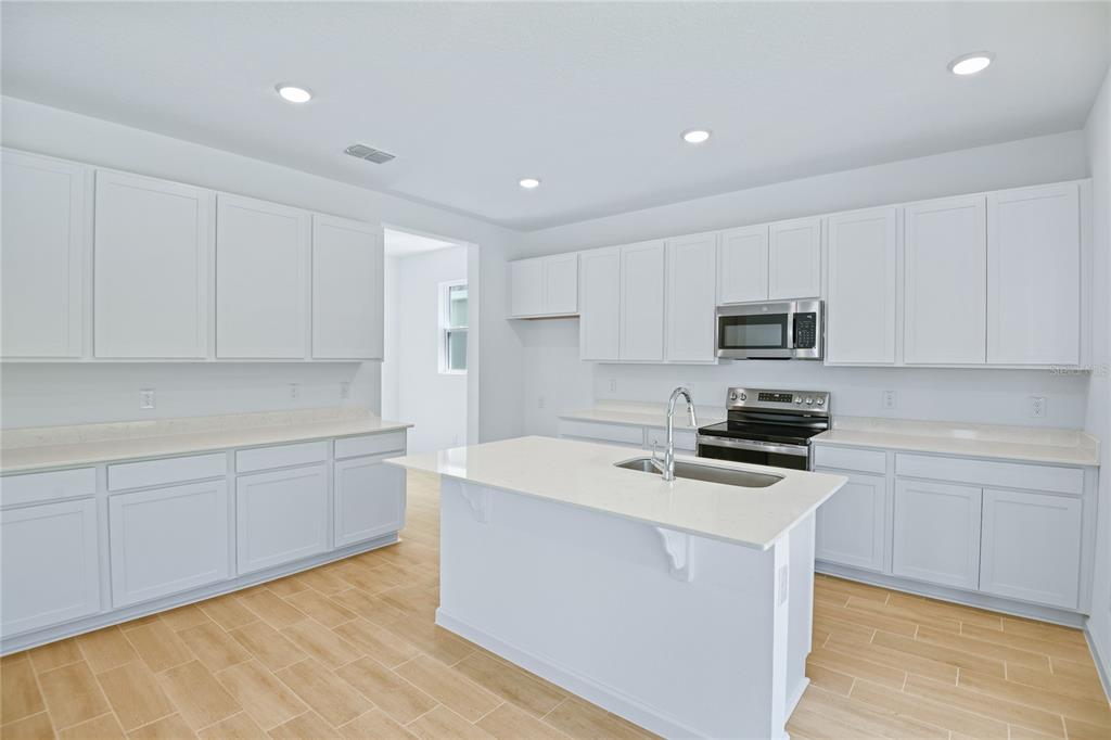 A kitchen features white cabinets, light countertops, a central island, and wood-look tile flooring — 6168 SW 64TH TERRACE, OCALA, FL