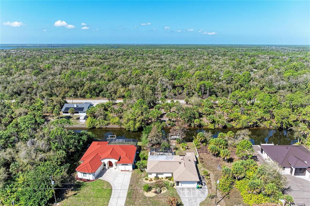 An aerial view shows two houses with pools situated along a canal near dense woods — 3123 COMO STREET, PORT CHARLOTTE, FL