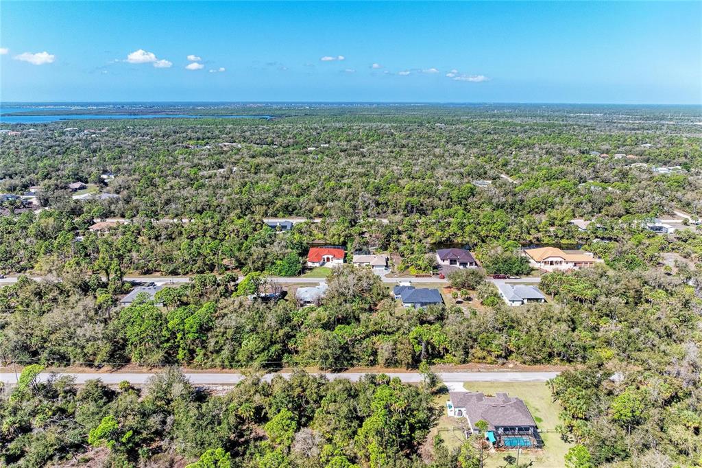 An aerial view shows several houses surrounded by dense trees and vegetation under a blue sky — 3123 COMO STREET, PORT CHARLOTTE, FL
