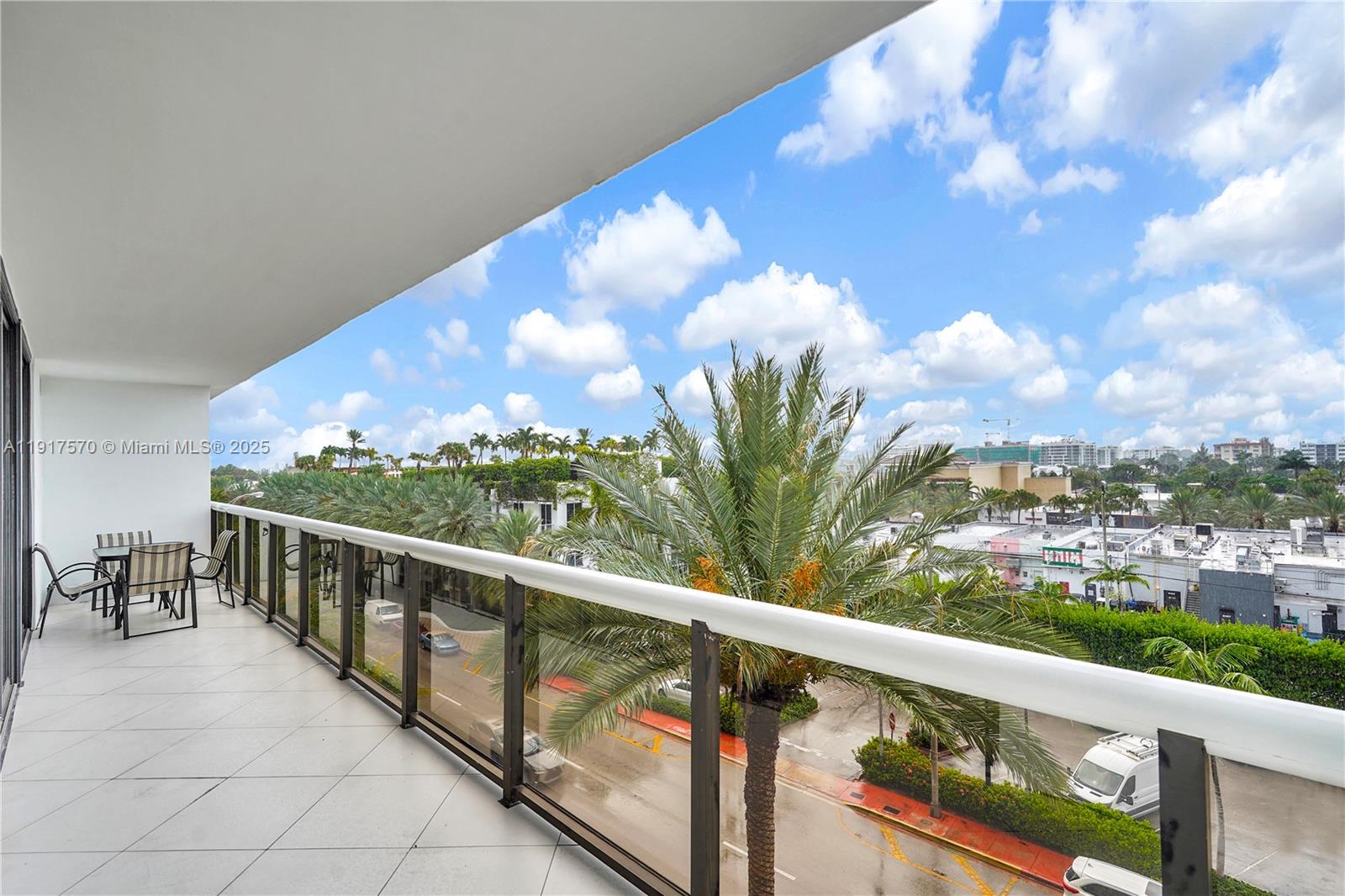 A balcony with tiled flooring, glass railings, and outdoor furniture overlooks a street and palm trees — 9455 Collins Ave # 603, Surfside FL 33154, SURFSIDE, FL