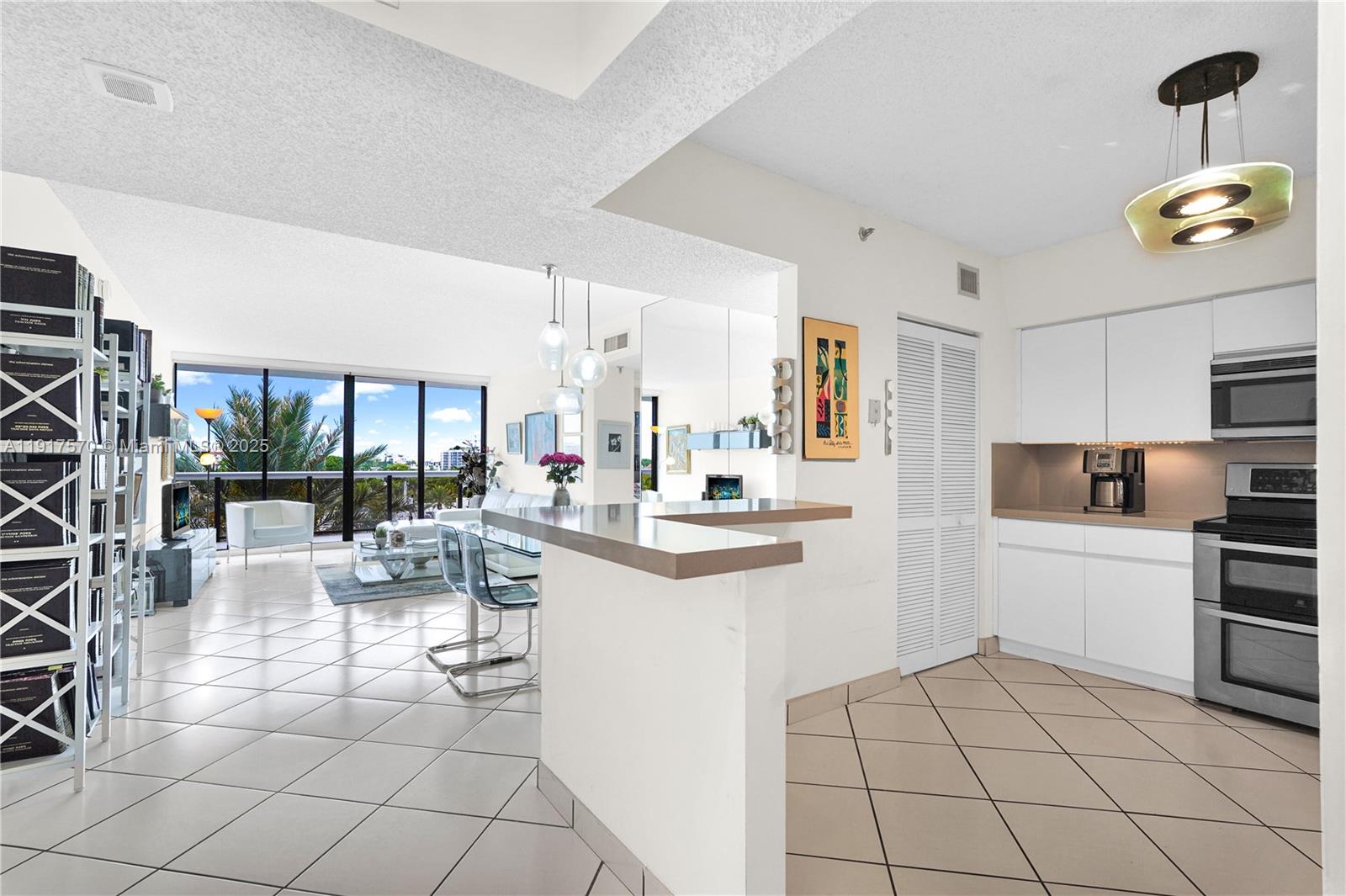 A kitchen with white cabinets and a breakfast bar opens into a bright living area — 9455 Collins Ave # 603, Surfside FL 33154, SURFSIDE, FL