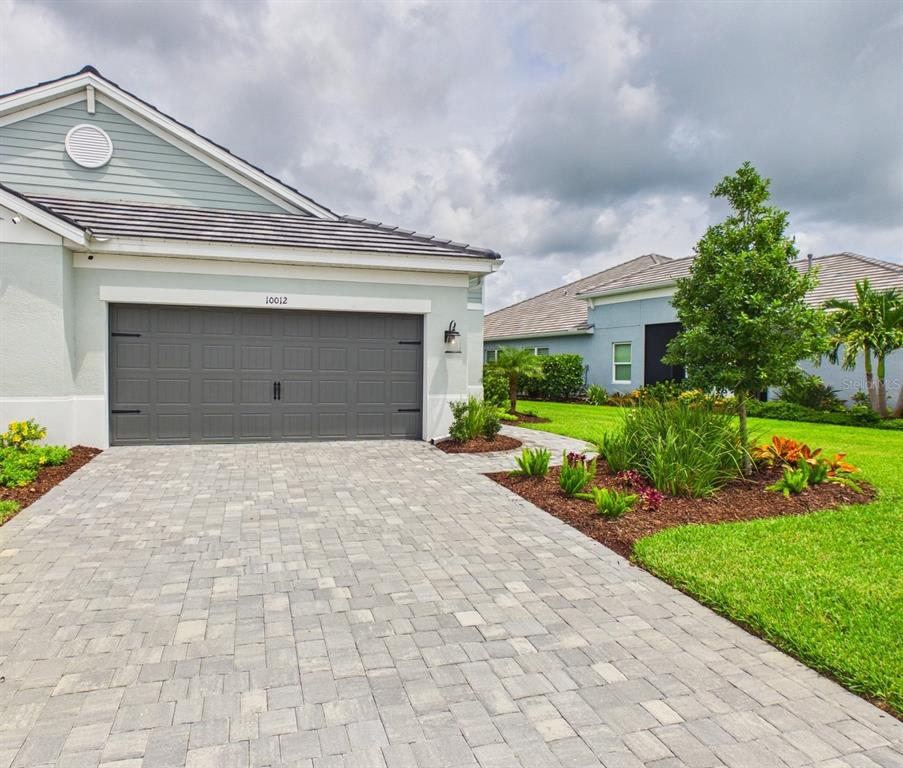 A paved walkway leads to the covered entryway of a light-colored house with landscaping — 10012 LAKE WALES CIRCLE, SARASOTA, FL
