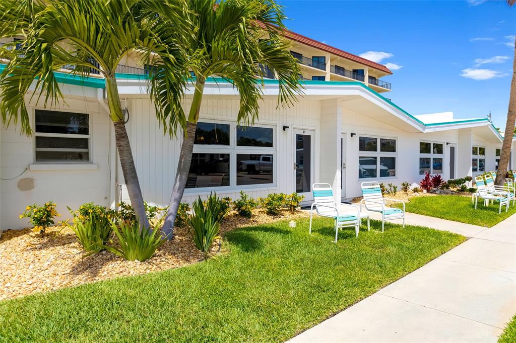 A white single-story building exterior features a palm tree, lawn, and outdoor patio chairs — 6334 MIDNIGHT PASS ROAD UNIT 41, SARASOTA, FL