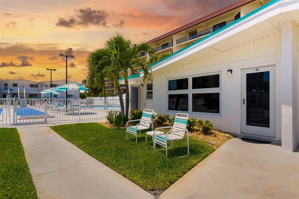 A white building exterior features a patio with two chairs, a palm tree, and pool access — 6334 MIDNIGHT PASS ROAD UNIT 41, SARASOTA, FL