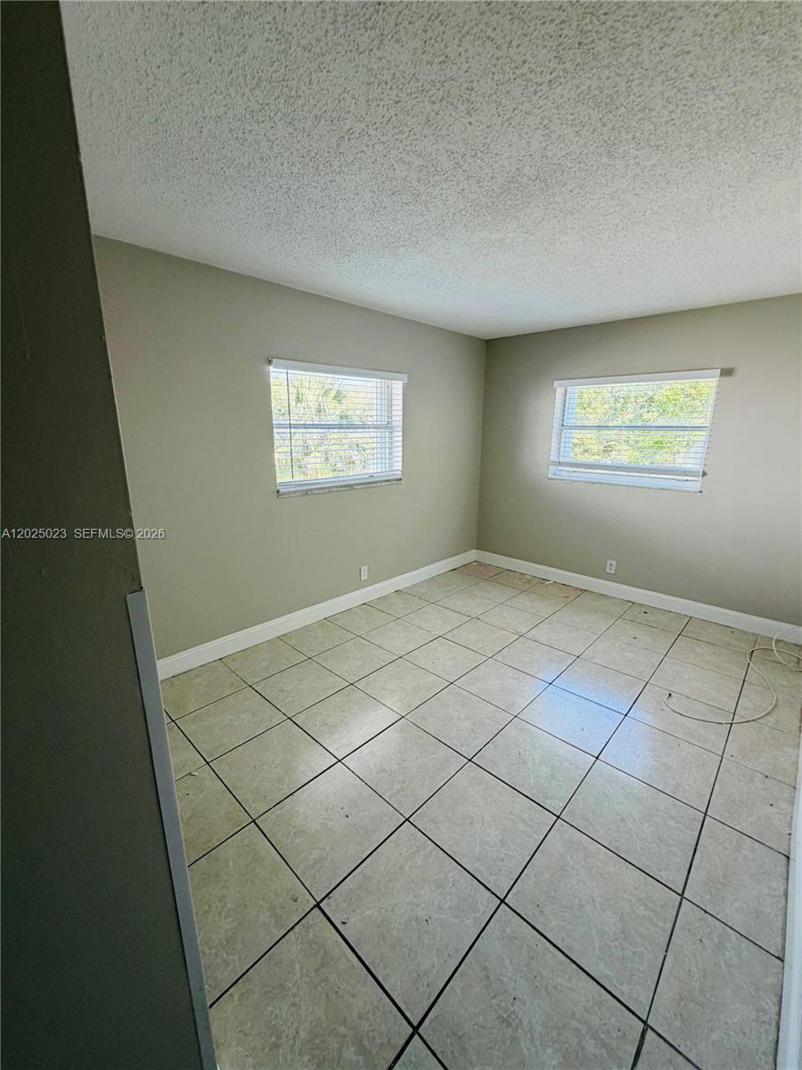 An empty room features light-colored tile flooring, beige walls, and two windows with blinds — 331 NW 42ND CT # 101, Pompano Beach FL 33064, POMPANO BEACH, FL