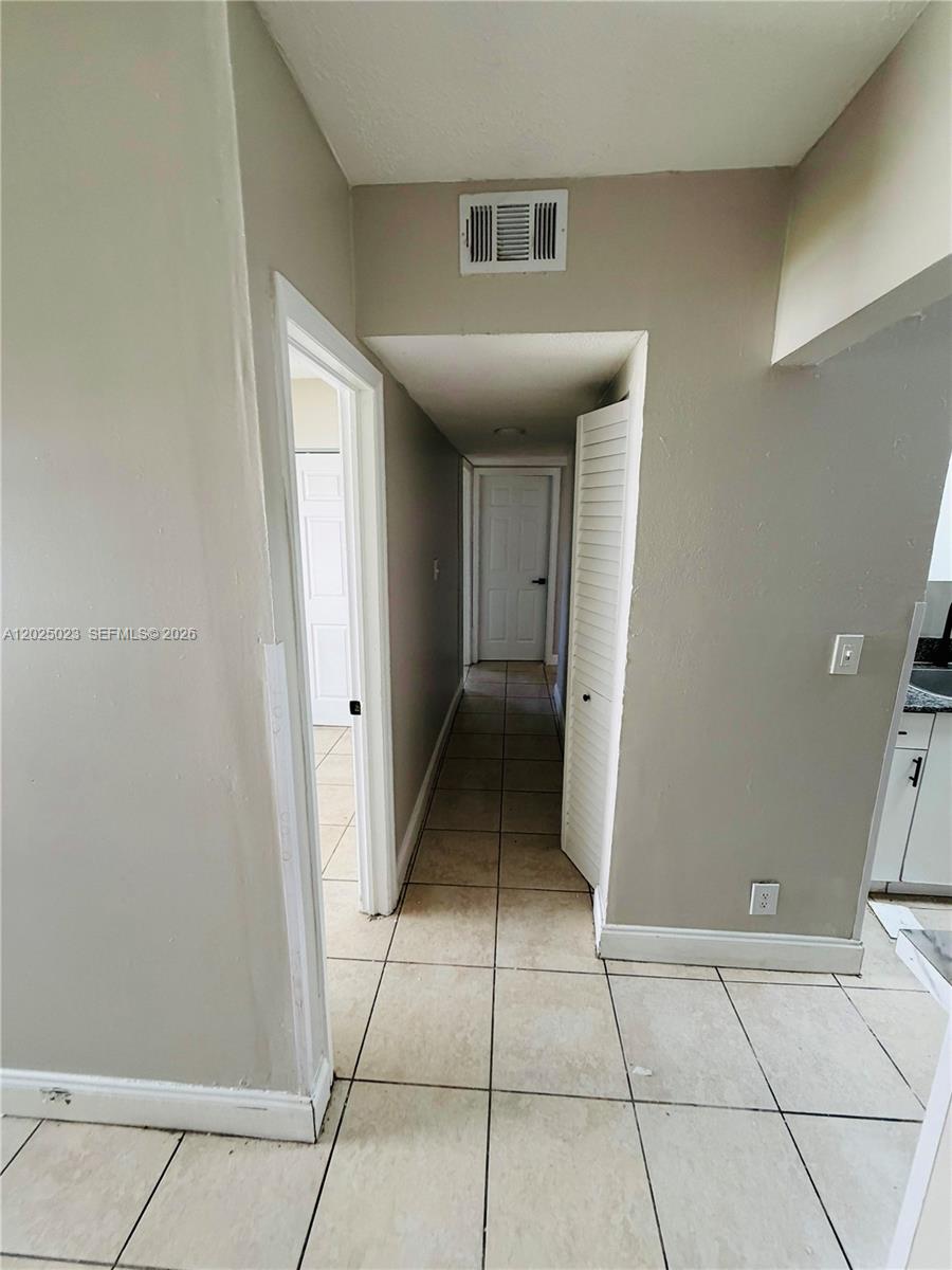 A hallway with beige walls and light-colored floor tiles leads to a closed door — 331 NW 42ND CT # 101, Pompano Beach FL 33064, POMPANO BEACH, FL