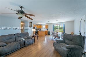 A living room with gray reclining furniture, wood-look flooring, and an open-concept kitchen — 1500 Jay Ter, La Belle FL 33935, LA BELLE, FL