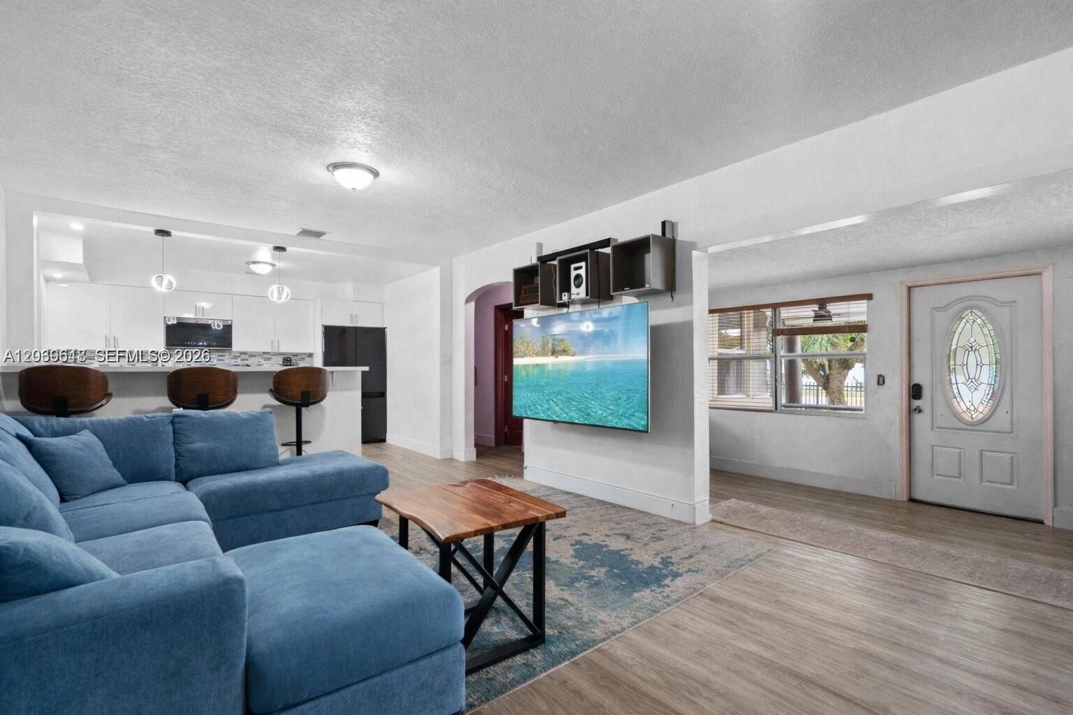 A living room features a blue sectional sofa, a wall-mounted television, and an open kitchen — 65 NW 118th St, Miami FL 33168, MIAMI, FL